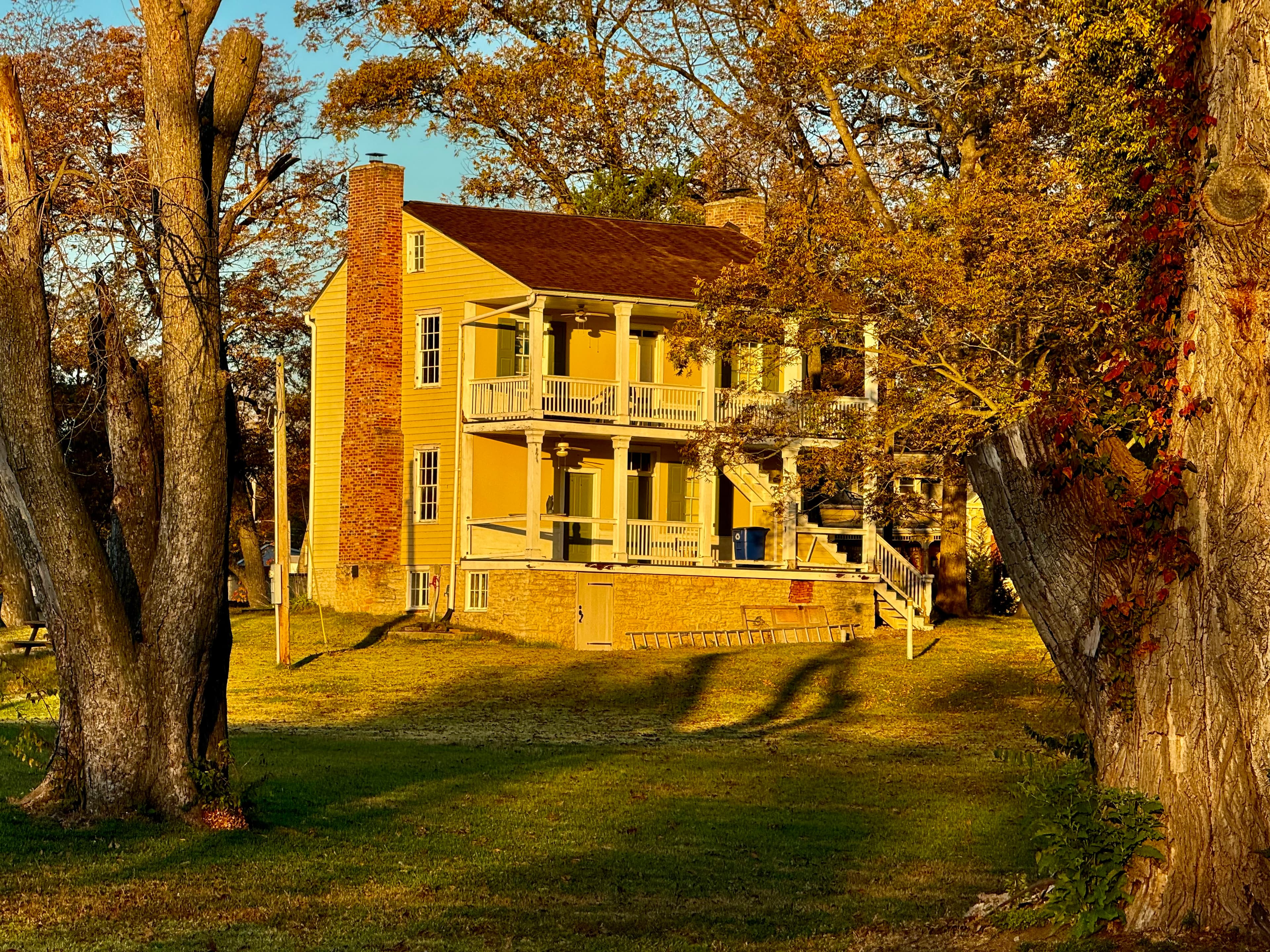 A historic yellow house surrounded by trees and autumn foliage.