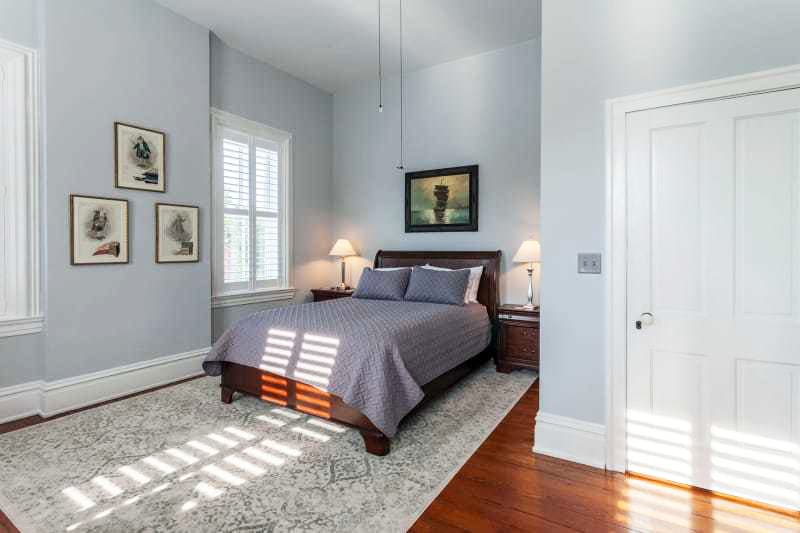 A serene bedroom featuring a queen-sized bed, two lamps, and framed artwork on light blue walls.